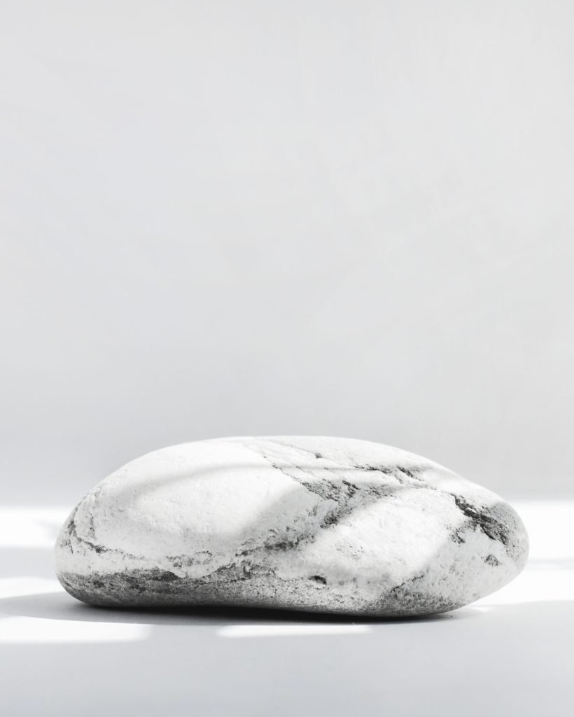 Background for cosmetics in natural white-gray color. Stone podium on a white background with hard shadows.